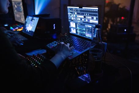 Hände steuern ein Mischpult vor Bildschirmen mit bunten grafischen Anzeigen.