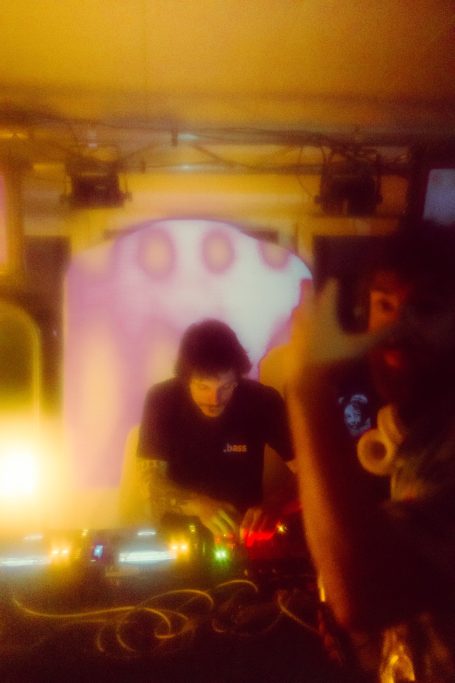 DJ bei einer Live-Performance, mit bunten Lichtern und einer person, die das Publikum aufnimmt.