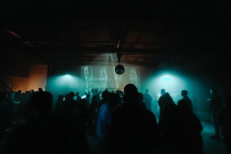 Menschenmenge in einem dunklen Raum mit bunten Lichtern und einer Discokugel.