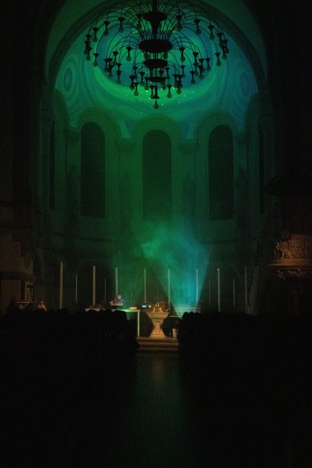 Dunkler Innenraum mit grünlich beleuchteten Wänden und einem zentralen Podium.