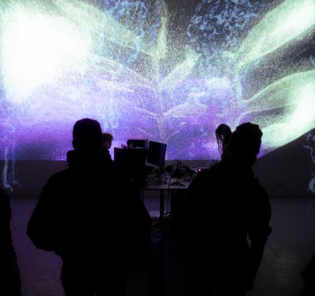 Silhouetten vor einer bunten, abstrakten Lichtinstallation an einer Wand.