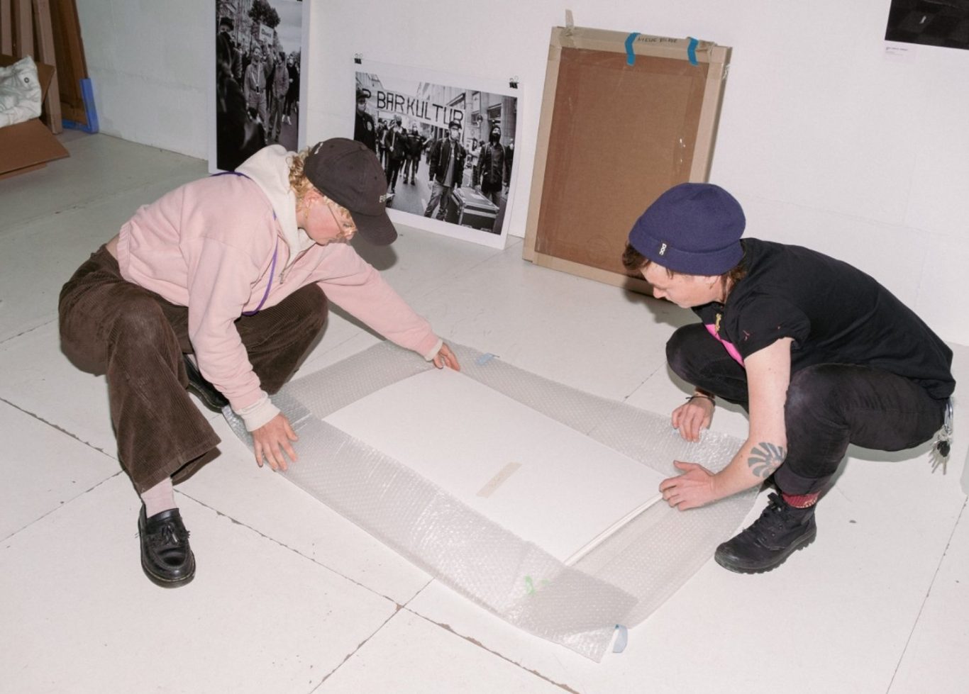 Zwei Personen legen ein großes Blatt Papier auf den Boden in einem kreativen Raum.