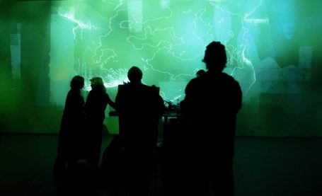 Menschen stehen vor einer leuchtenden, grünen Projektion an einer Wand.