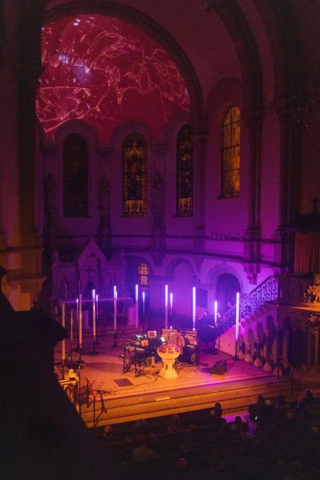 Bühne in einer Kirche mit bunten Lichtern und musikalischer Darbietung.